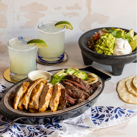 a plate of fajitas with guacamole and margaritas